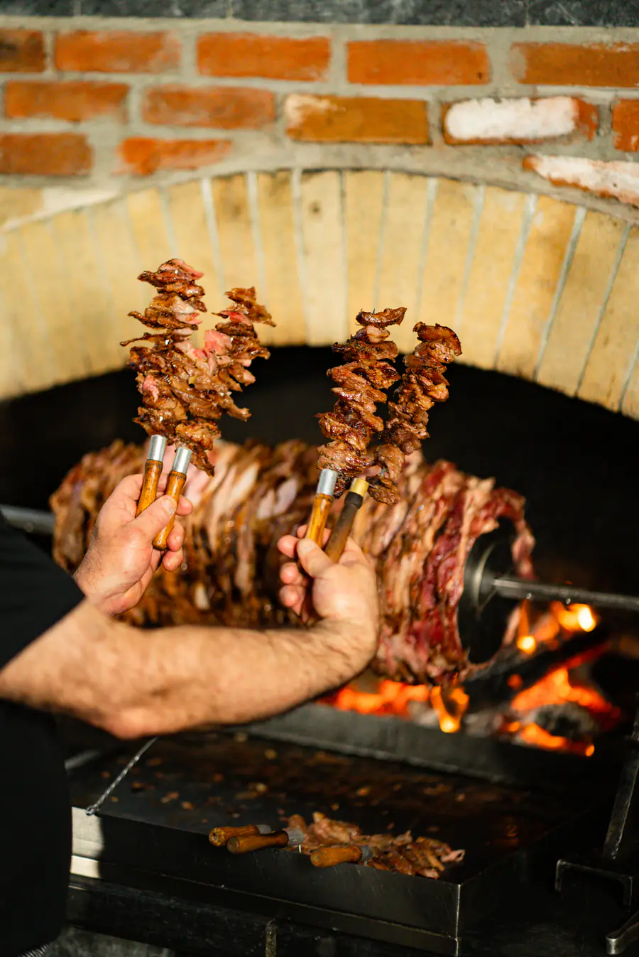 Ustanın elinde iki dolu cağ kebap şişi, arkada ocak ve alev